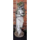 A weathered composite garden statue, modelled as a young woman with hands clasped to loose robes,