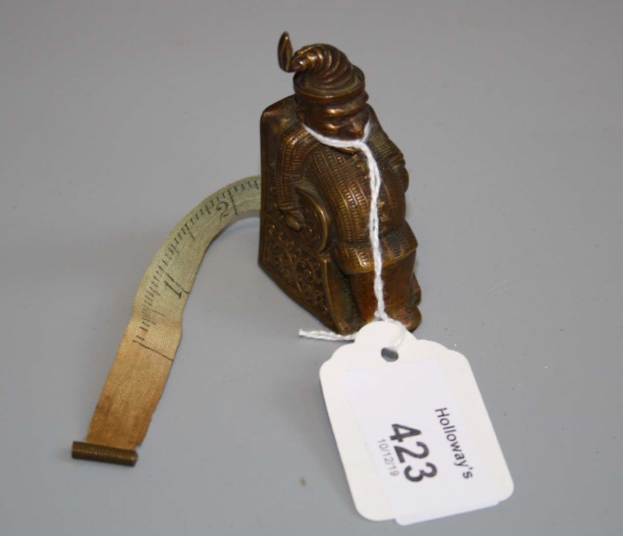 A 19th century brass 'Mr Punch' figural tape measure, the corpulent, seated figure of Mr Punch