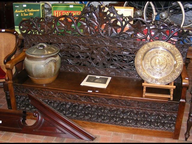 An antique heavily carved settle with hinged lift-