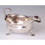 A GEORGE III SILVER SAUCE BOAT having a boat-shaped body with a scrolled edge on thee shaped feet
