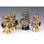 A COLLECTION OF FOUR BRASS OIL FILLED TAIL LAMPS having double tier chimneys having clear and red