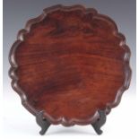 A GEORGE III FIGURED MAHOGANY DRINKS TRAY with pie crust edge and baize underside 28.5cm diameter.