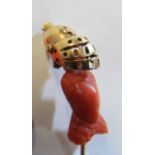 A 19th Century stick pin with carved coral terminal of a knight with yellow metal hinged helmet