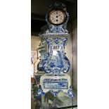 A tall Delft pottery clock in the form of a longcase clock with scene of a girl by river and boats