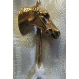 A yellow metal stick pin horses head with ruby eyes