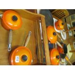 A set of Le Creuset orange saucepans on hanging shelf