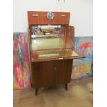 A 1970's walnut effect cocktail cabinet with hinged and lifting front to reveal mirrored and lit