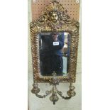 A pair of ornate brass mirrors with female heads to top and embossed leaf frames each with three