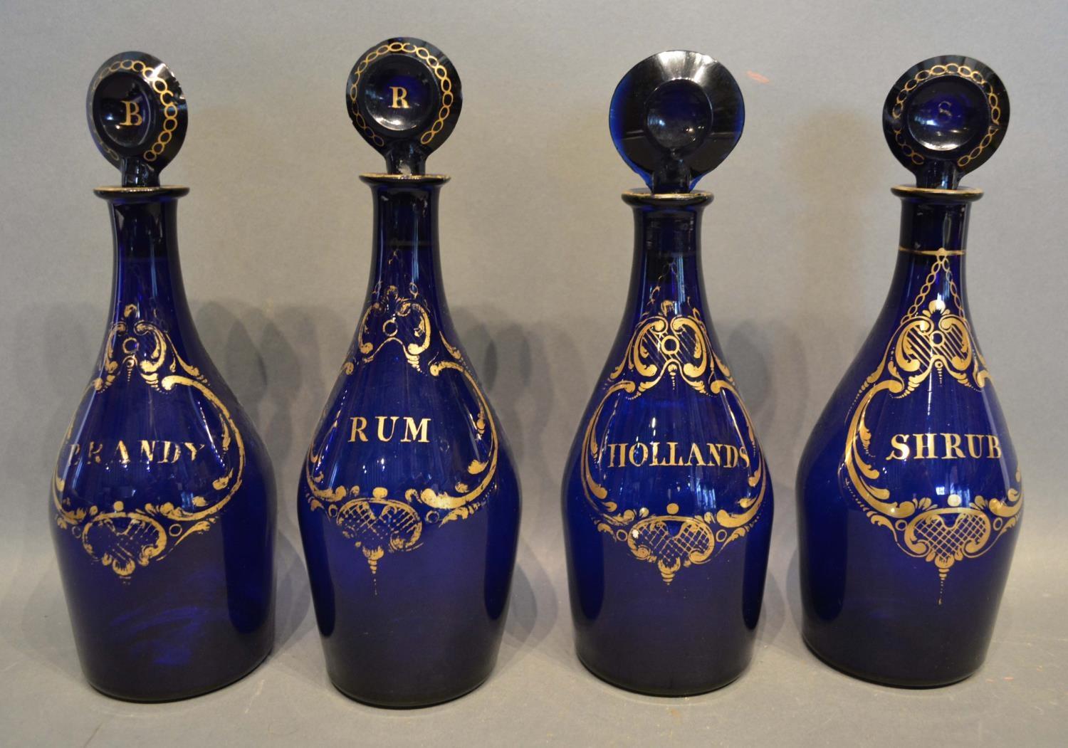 A Set Of Four Early 19th Century Blue Glass Decanters, all highlighted with gilt, Brandy, Rum,