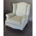 An Upholstered Wing Back Arm Chair with turned reeded legs, brass caps and castors