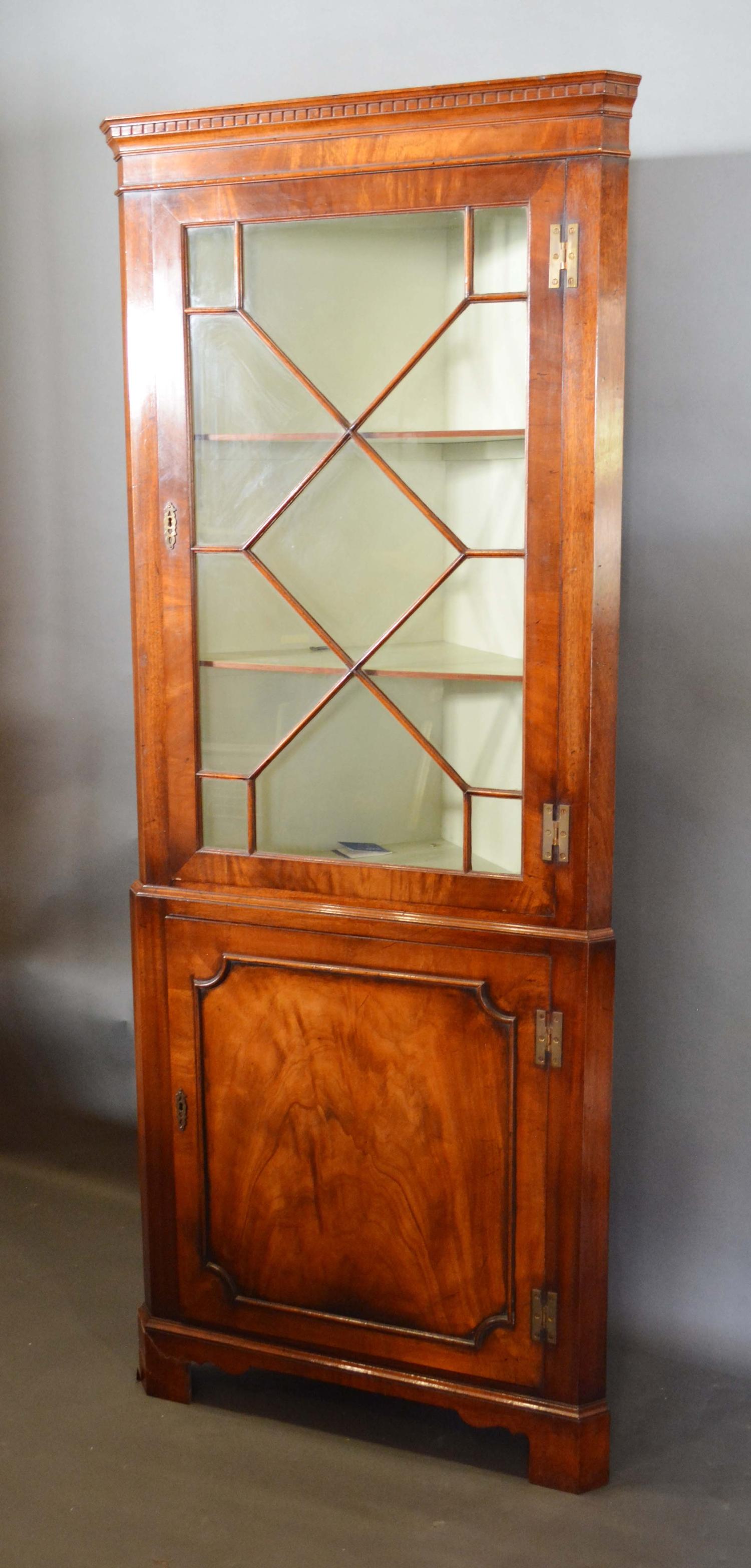 A Mahogany Standing Corner Cabinet with an astragal glazed door enclosing shelves, the lower section