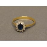 An 18 Carat Yellow Gold Sapphire and Diamond Cluster Ring set with oval sapphire surrounded by