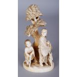 A SIGNED JAPANESE MEIJI PERIOD IVORY OKIMONO OF A LADY & HER CHILDREN, beneath an overhanging pine