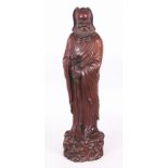 A 20TH CENTURY CHINESE CARVED HARDWOOD FIGURE OF AN IMMORTAL, standing on a knarled plinth, the