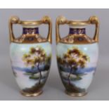 A PAIR OF NORITAKE TWO HANDLED VASES painted with a lakeside scene, 10in high.