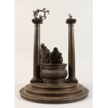 AN UNUSUAL CAST METAL SCULPTURE, two monks stood beside a well, on a stepped circular base. 13ins