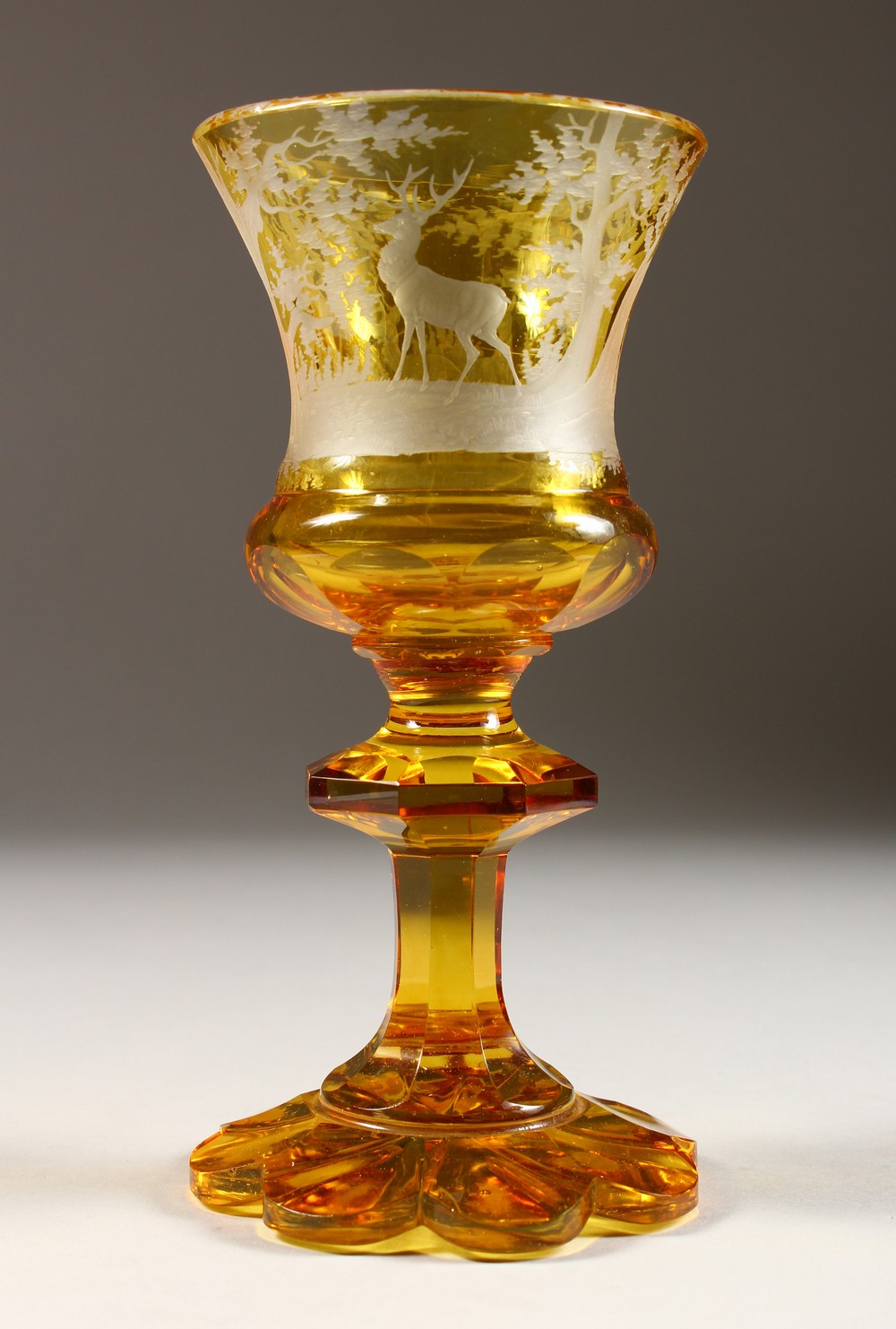 A BOHEMIAN AMBER CUT GOBLET, engraved with deer in a wood. 7ins high.