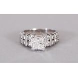 A 14CT WHITE GOLD DIAMOND PRINCESS CUT RING with stepped diamond shoulders.