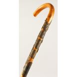 AN ALPINE WALKING STICK, with crook handle, the shaft with applied brass plaques. 36ins long.