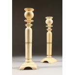 A PAIR OF ART DECO IVORY CANDLESTICKS on square bases. 10ins high.