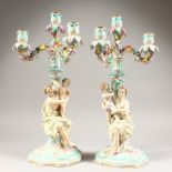 A PAIR OF CONTINENTAL PORCELAIN CANDELABRA, each with scrolling branches and figural base. 18ins