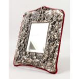 AN ORNATE STRUT MIRROR, the frame cast with cherubs and flowers, stamped STERLING SILVER. 10.5ins