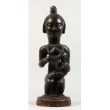 A CARVED TRIBAL FIGURE feeding a baby. 1ft 5ins high.