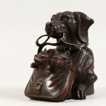 A CARVED WOOD INKWELL, modelled as a dog holding a bag of puppies in its mouth. 5ins high.