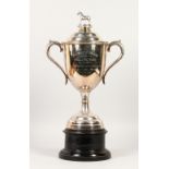 A LARGE EQUESTRIAN TWIN HANDLED TROPHY CUP, the cover with horse finial, on an ebonised base.