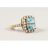 A 9CT GOLD EMERALD CUT BLUE TOPAZ AND SEED PEARL RING.
