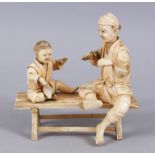 A GOOD QUALITY JAPANESE IVORY OKIMONO GROUP, father and son sat upon a bench, the father holding a