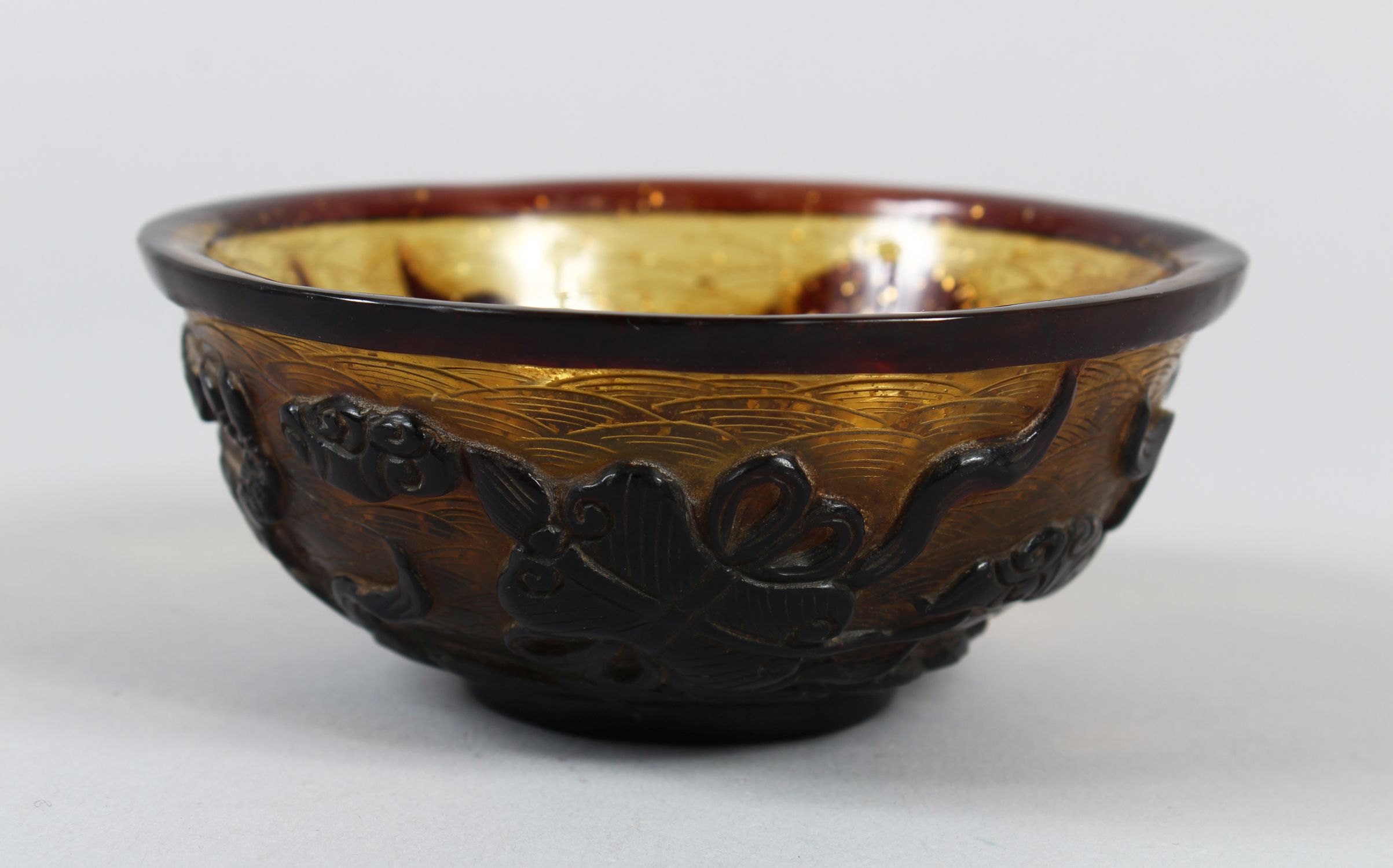A CHINESE PEKING AMBER GLASS RICE BOWL, with gilt speck inclusions, carved decoration of four Taoist