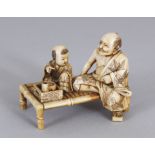 A SMALL JAPANESE MEIJI PERIOD STAINED IVORY OKIMONO OF A FATHER & SON, both seated on a low bamboo-