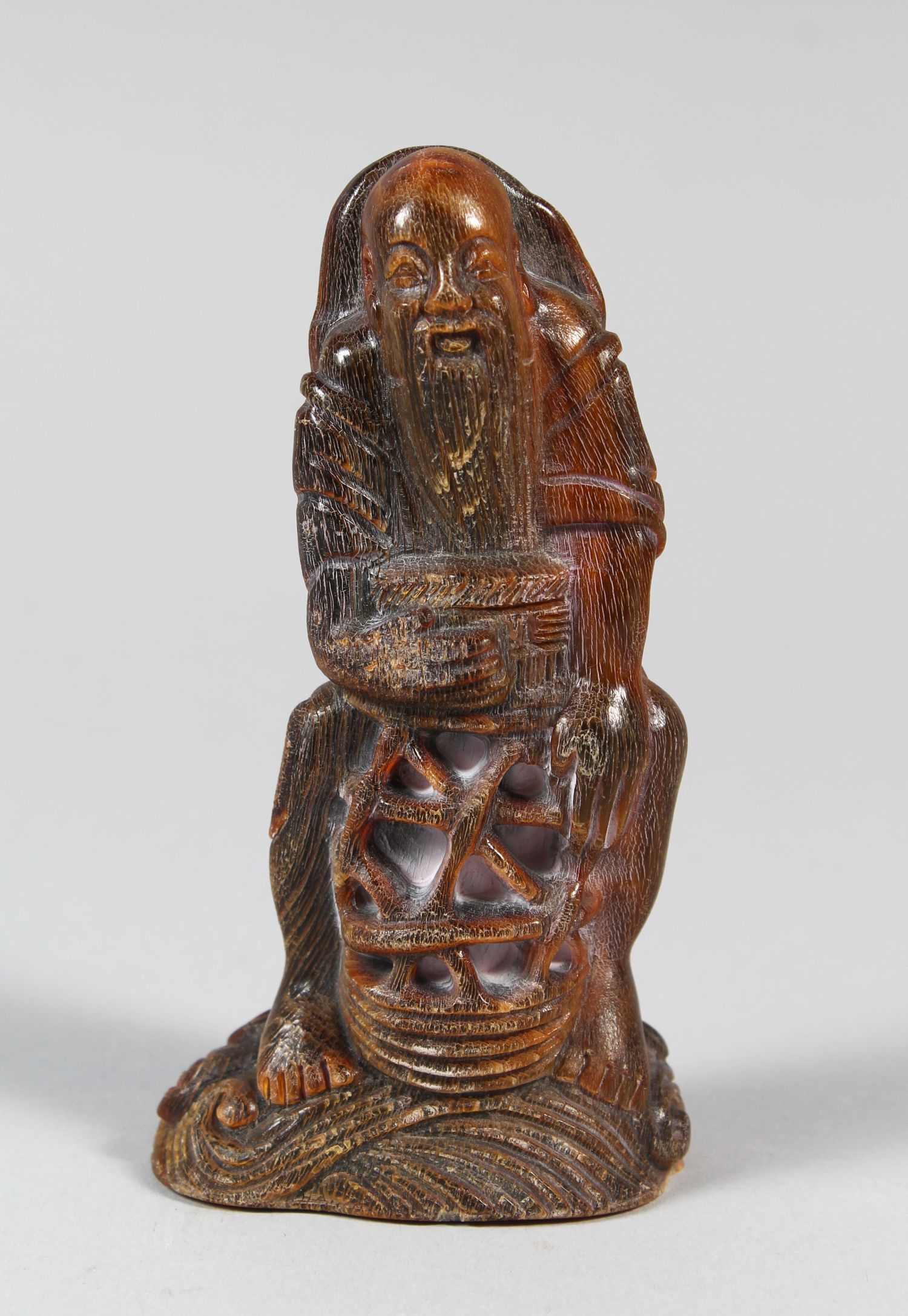 A CHINESE CARVED HORN FISHERMAN FIGURINE, seated upon a rocky outcrop, 11 cm high 5.5 cm wide.