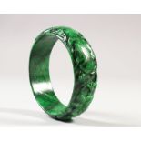 A CHINESE JADE BANGLE, carved to the rounded rim with foliage, the green stone with black