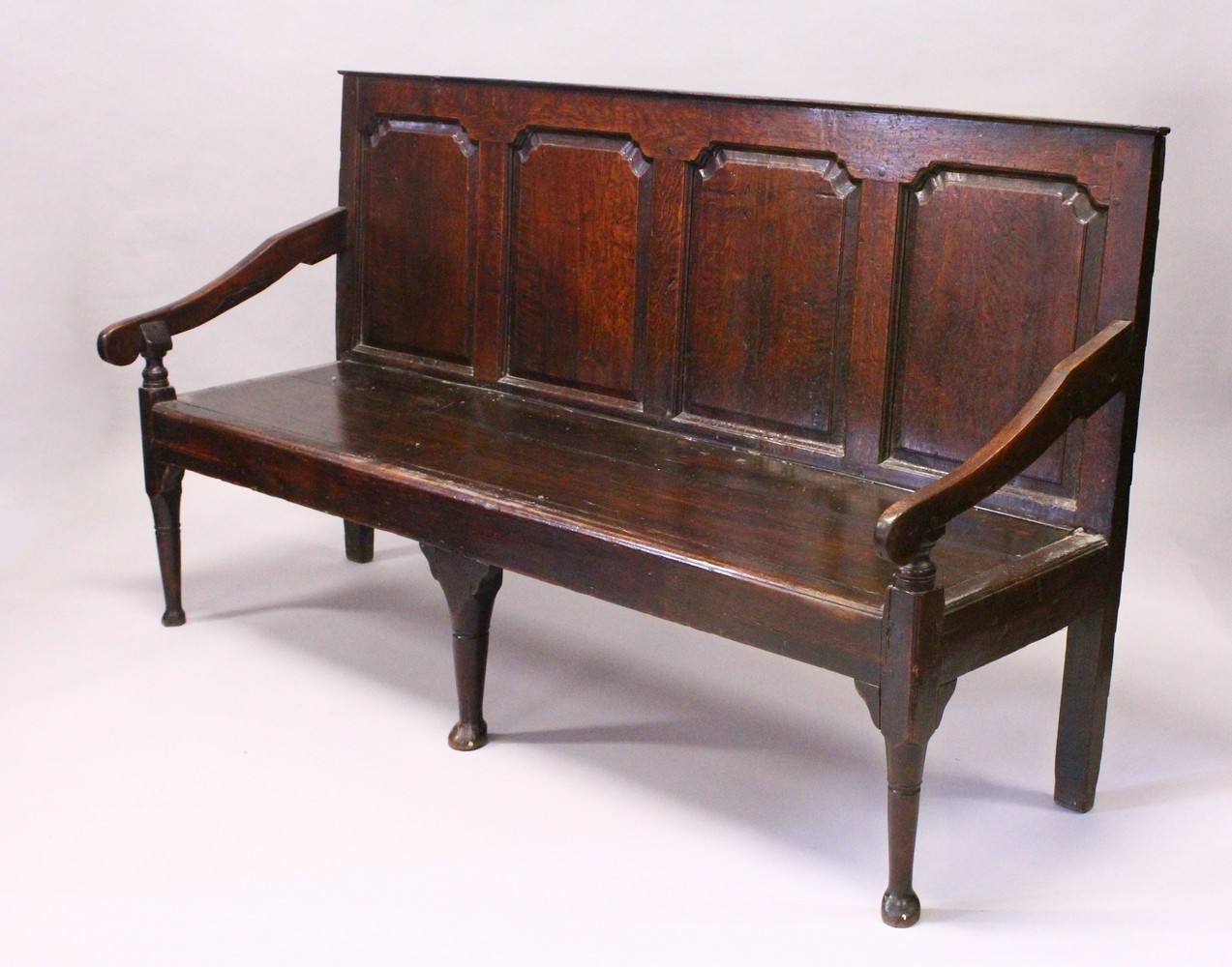 AN 18TH CENTURY OAK SETTLE, with a four panel back, curving arms, solid seat, on cabriole front