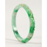 A LARGE CHINESE GREEN AND WHITE JADE BANGLE, with carved decoration. 10.5cms diameter.