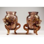 AN UNUSUAL PAIR OF CONTINENTAL MOTTLED RUBY VASES, with gilt decoration, on three curving legs.