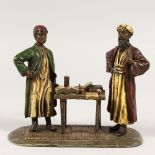 A COLD PAINTED BRONZE, modelled as two men stood beside a table covered with books. 14cms high.