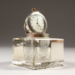 A SQUARE CUT GLASS TABLE INKWELL, with inset silver watch. Birmingham 1907. 7cms square.