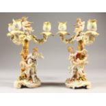 A PAIR OF CONTINENTAL PORCELAIN CANDELABRA with three branches, cupids, mother and cupid. 23cms