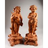 A PAIR OF VICTORIAN STYLE TERRACOTTA FIGURES, of a standing boy and girl holding fruit and leaves,