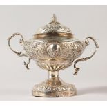 A CONTINENTAL SILVER TWO HANDLED CUP AND COVER with repousse decoration, masks and pineapple finial.