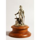 AN EARLY METAL CAR MASCOT, A MAN AT AN ANVIL. 11cms high, on a turned wooden base.