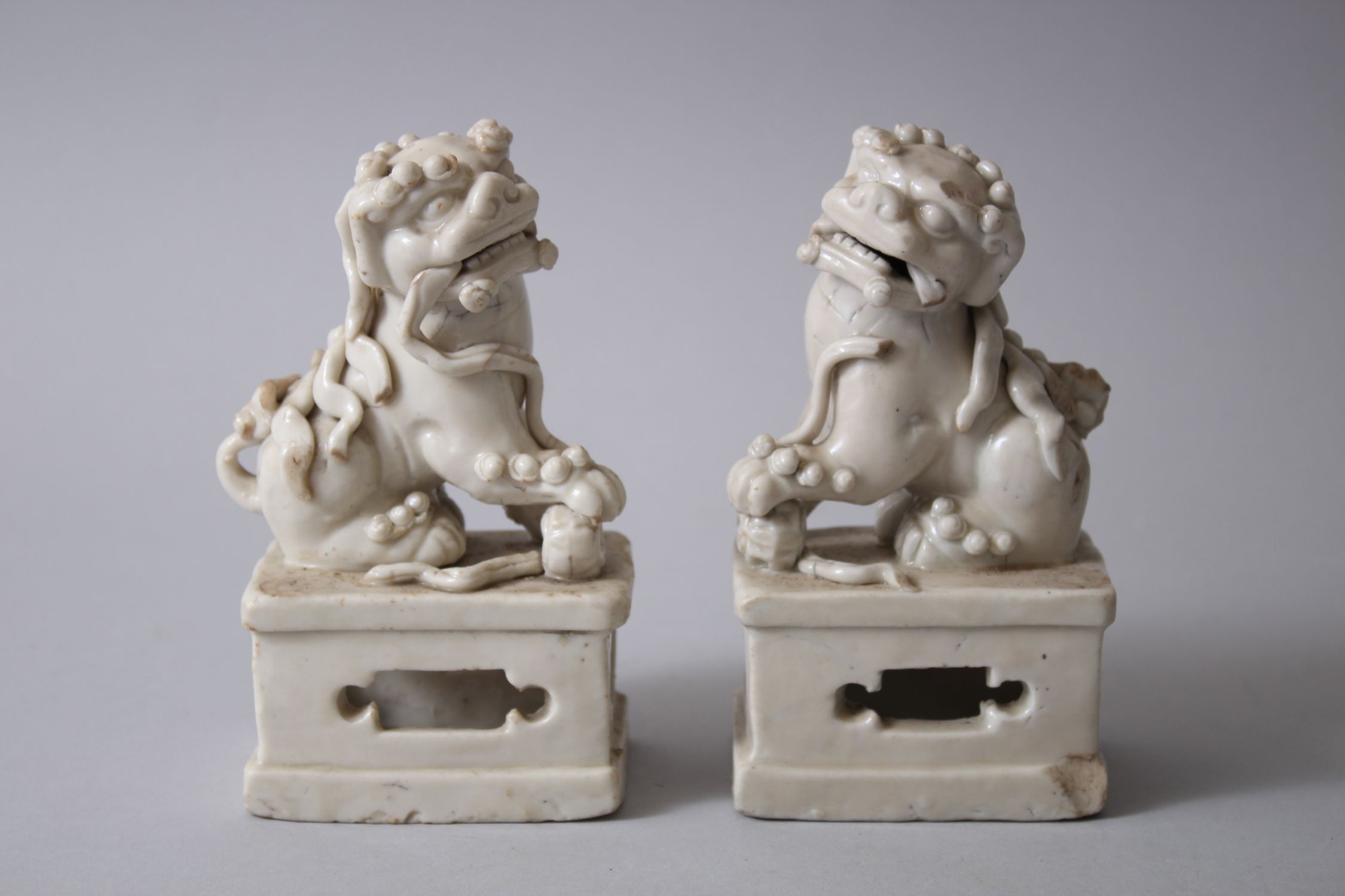PAIR OF 19TH CENTURY CHINESE CHINE DE BLANC / DEHUA LION DOG FIGURES, both seated upon pierced