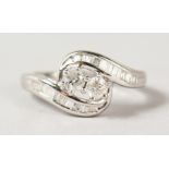 A 9CT WHITE GOLD TWO STONE DIAMOND CROSSOVER RING with baguette shoulders.