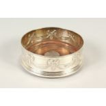 A SILVER CIRCULAR WINE COASTER the sides with ribbon motifs and a wooden base. 12cms diameter.