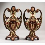A PAIR OF CONTINENTAL MAJOLICA TWO HANDLED VASES with scrolls and winged cupids. 40cms high.