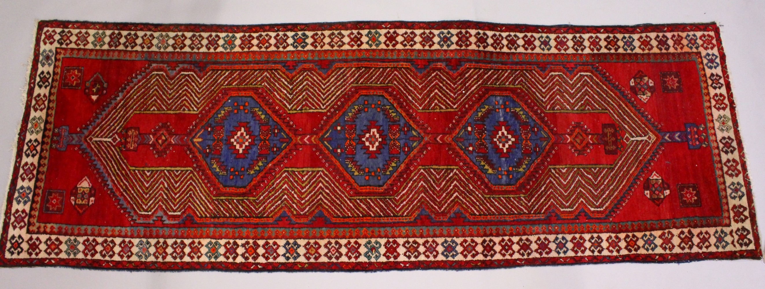 A PERSIAN LONG CARPET / RUNNER, bright red ground with three blue ground motifs in a stylized