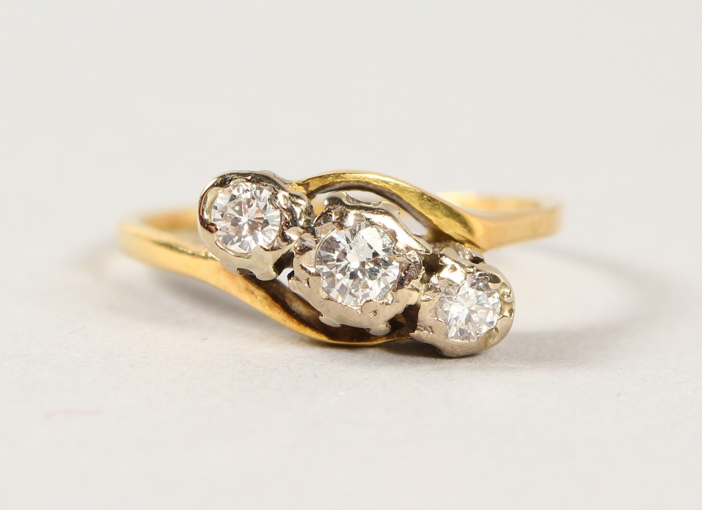 AN 18CT GOLD THREE STONE DIAMOND CROSSOVER RING.